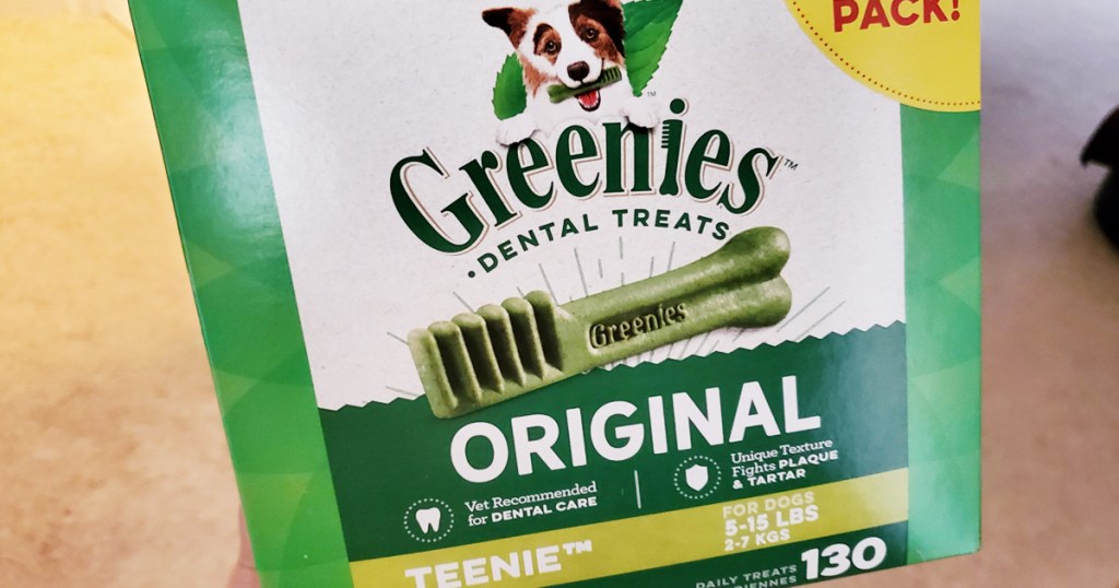 person holding up a green and white box of greenies original dog treats