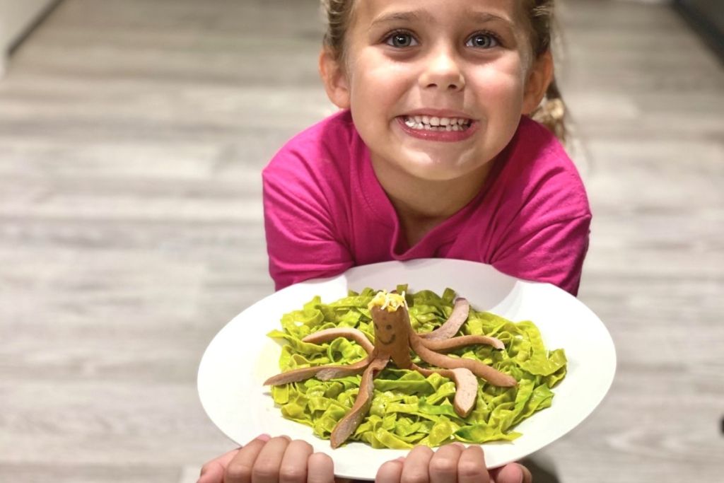 A little girl holding a plate with noodles and a hot dog