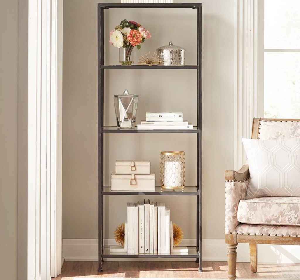 tall glass bookcase with bronzed metal frame in living room with trinkets and books on each shelf