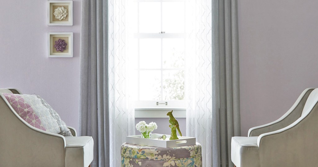 room with grey and white curtain panels with seating area and ottoman in front