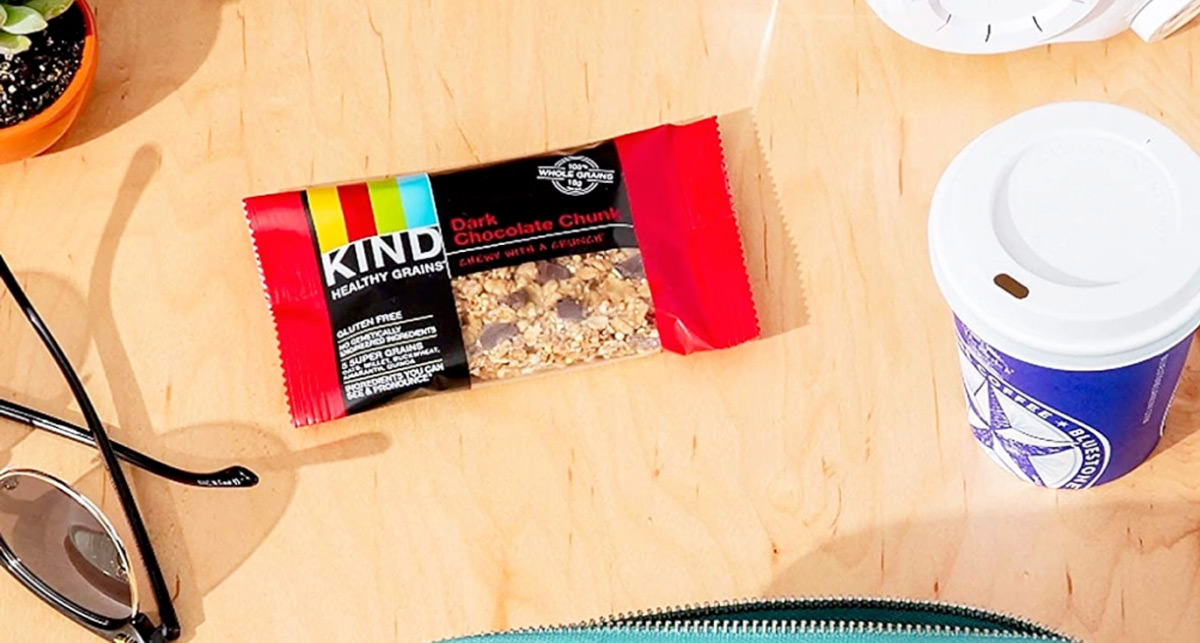 chocolate chunk flavor kind bar in red wrapper on table with coffee and sunglasses