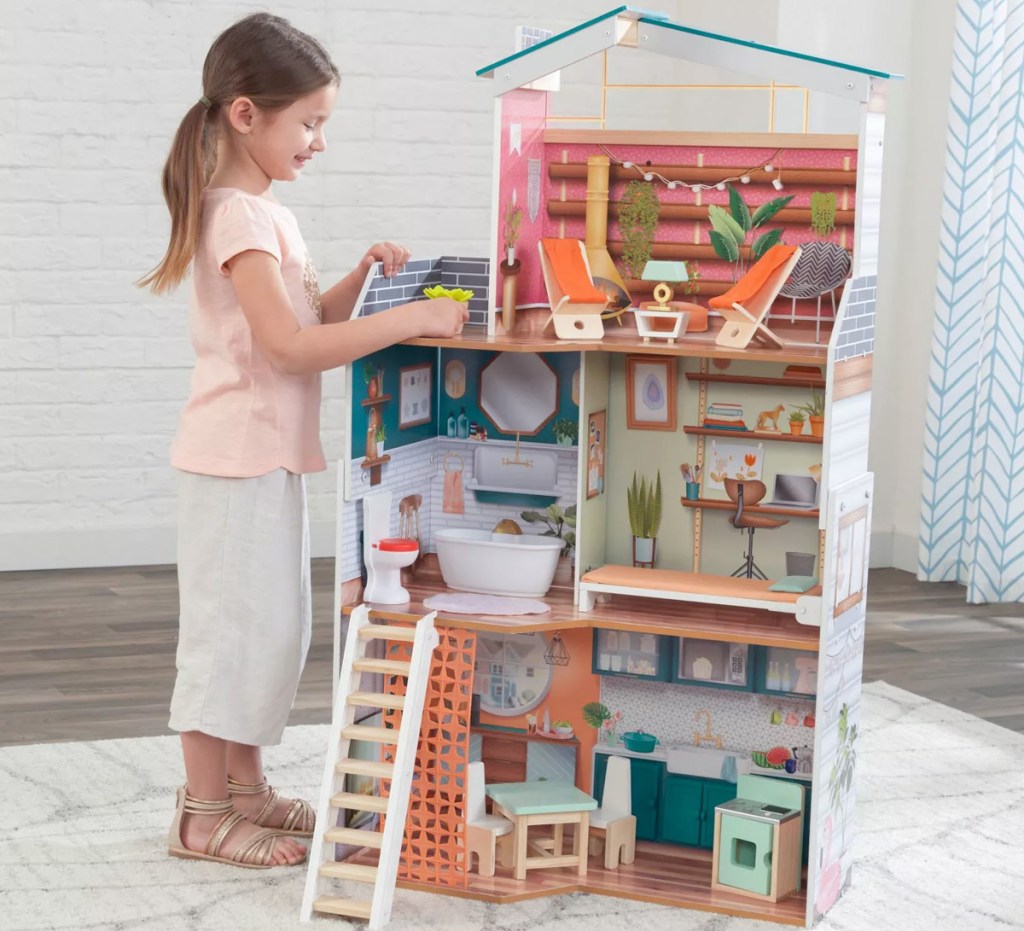 girl standing next to large dollhouse the same height as her, with furniture in each room