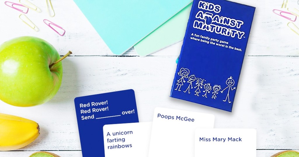 white and blue kids against humanity playing cards and box on white wood background with fruit around them