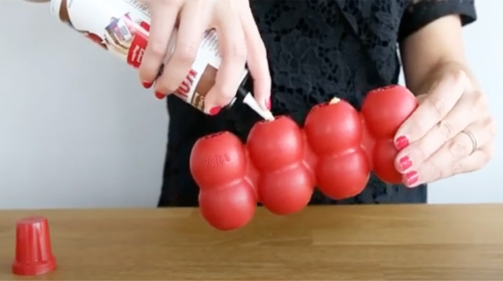 person spraying kong cheese into red toy