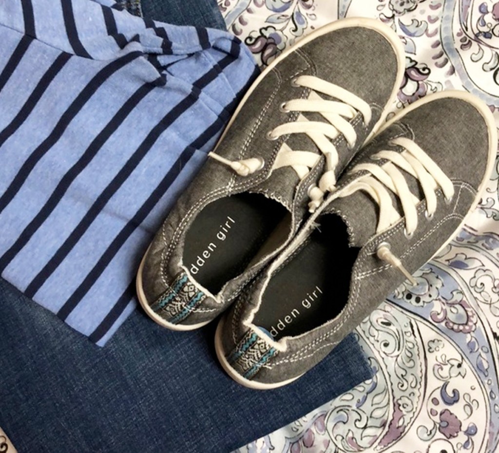 grey pair of slip on womens shoes on top of blue striped shirt and paisley print comforter