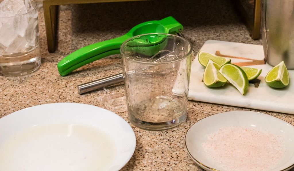 Sliced limes and a citrus juicer next to a glass and plates on a counter