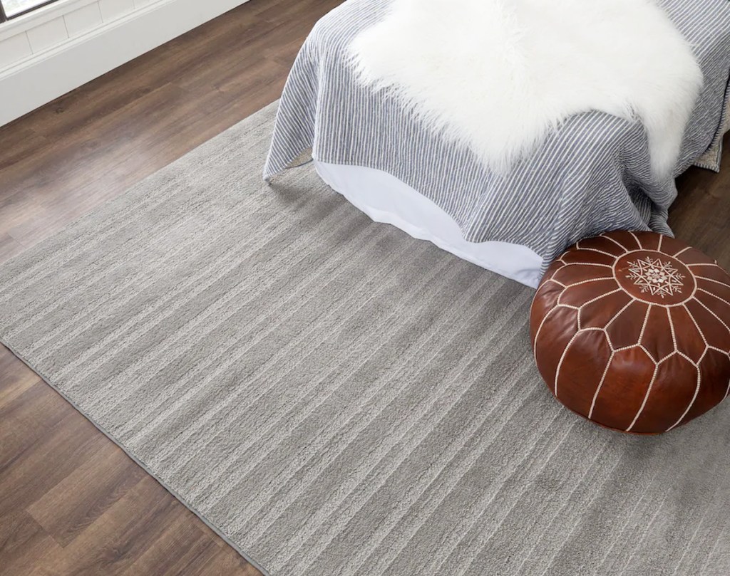 grey area rug under bed and ottoman on a hardwood floor