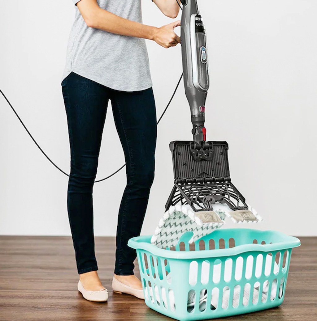 woman holding steam mop over blue laundry basket and pressing button to remove mop pad into basket