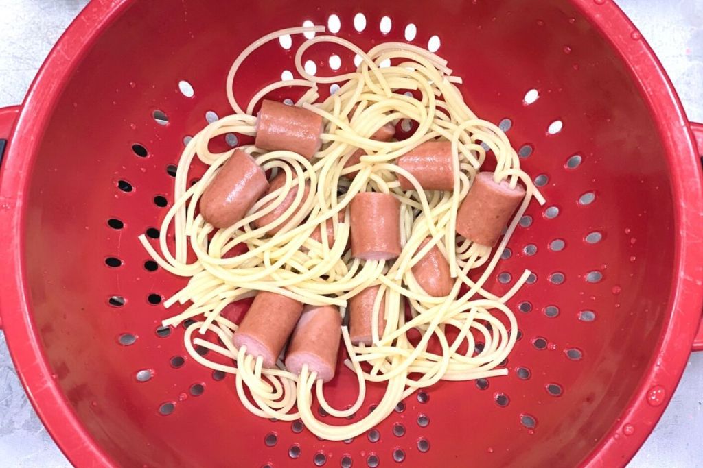 Hot dogs and noodles in a strainer