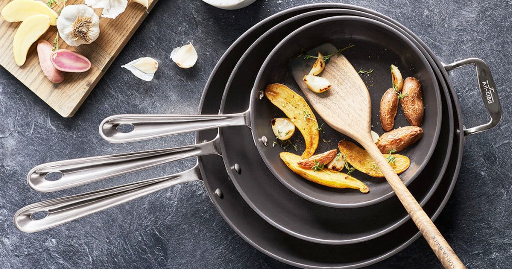 set of three black frying pans stacked into one another with roasted peppers and wooden spoon