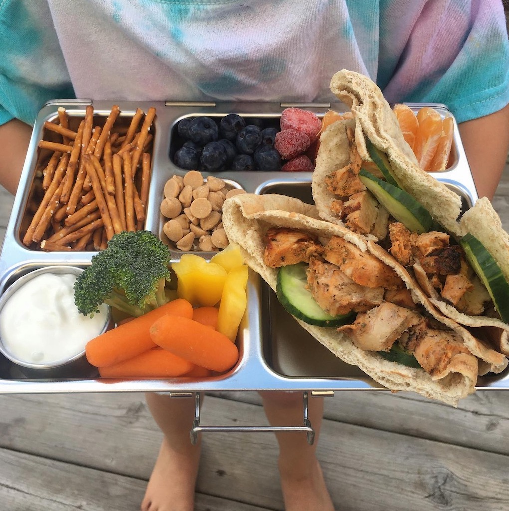 boy holding Planetbox lunch filled with veggies and pita sandwich 