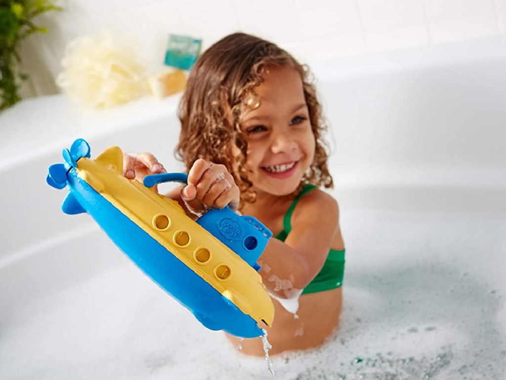 little girl playing in bubble bath with submarine toy