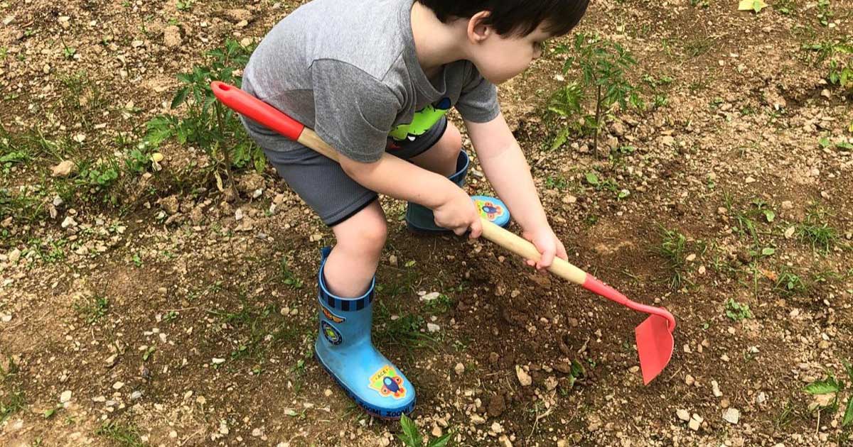 boy digging in the dirt with a small garden hoe