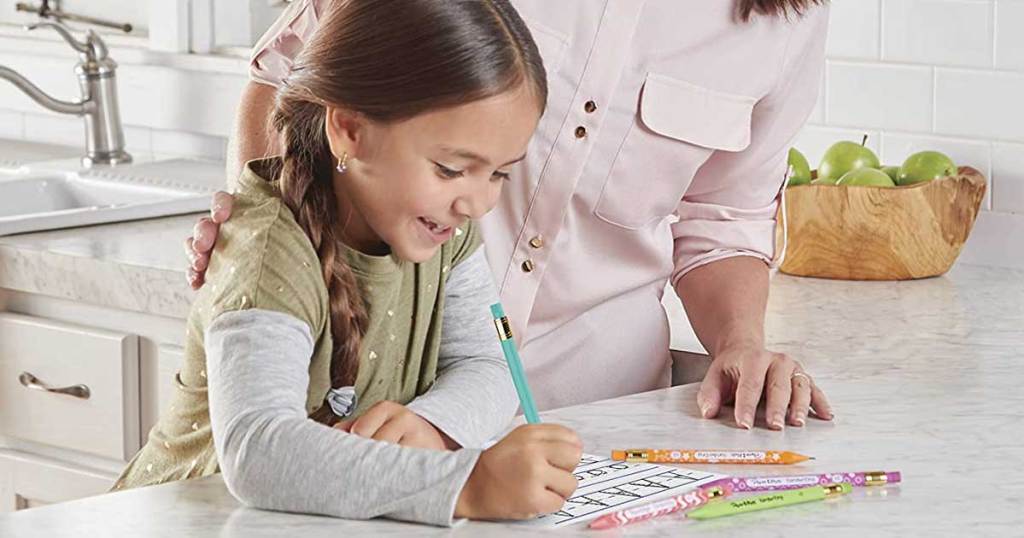 little girl writing on a table with pencils