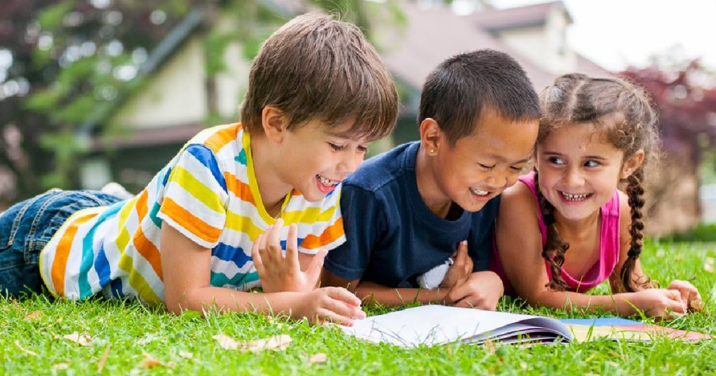 kids laying on grass looking through workbook 