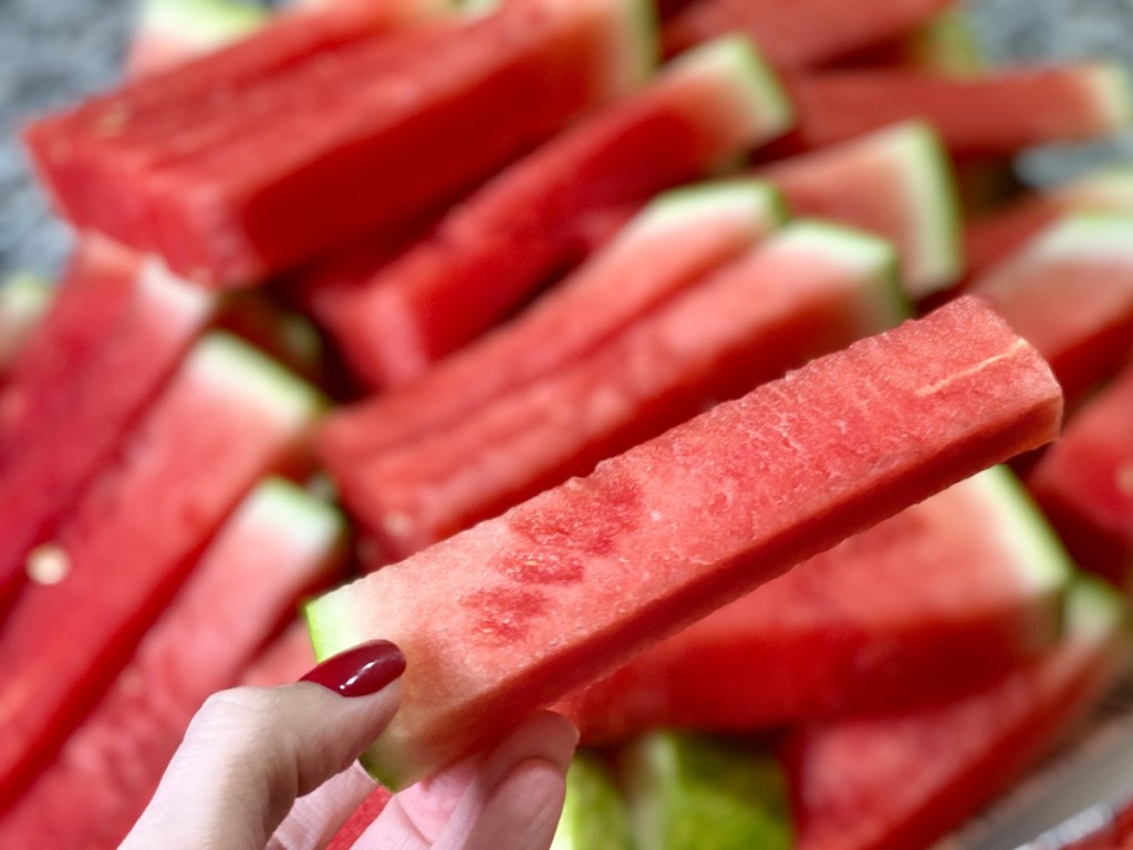 hand holding watermelon spear over tray of spears