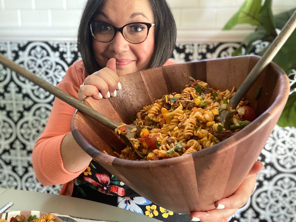 woman holding large wood bowl filled with taco pasta salad