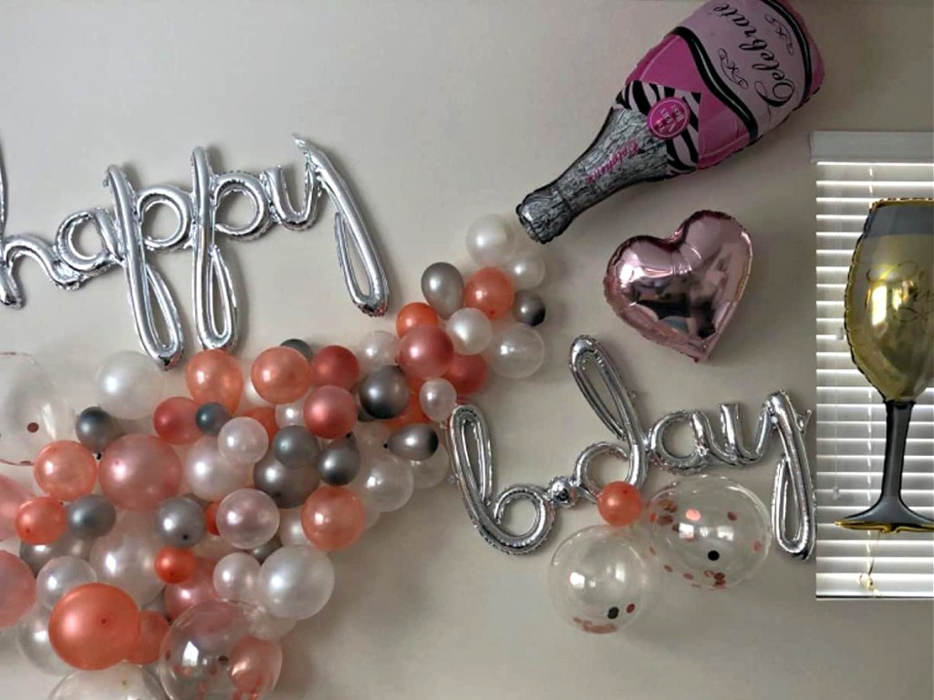 giant champagne bottle balloon and pink and gold balloon arch and "happy birthday" silver balloons on wall