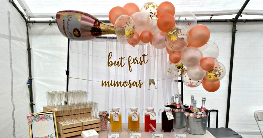 giant champagne bottle balloon and pink and gold balloon arch at mimosa party table