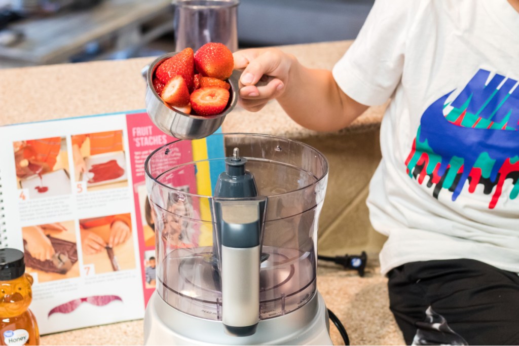 boy pouring strawberries into a food processor