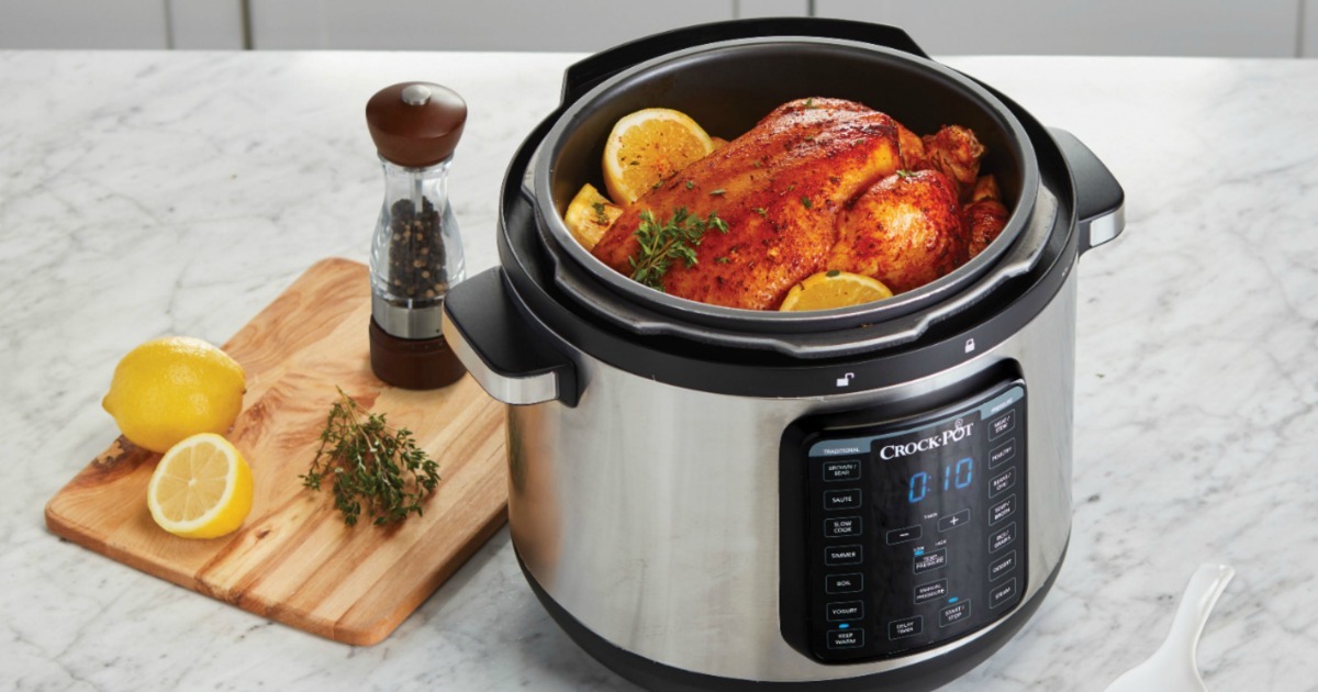 Large pressure cooker on counter with chicken and lemons inside, near wooden cutting board