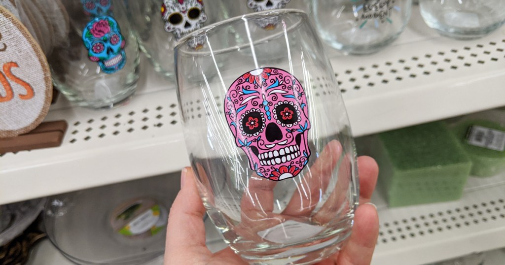 person holding a stemless wine glass with a pink sugar skull printed on it