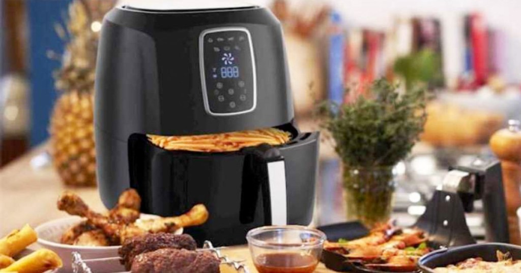 black air fryer with basket open showing french fires inside, sitting on kitchen counter surrounded by other fried foods