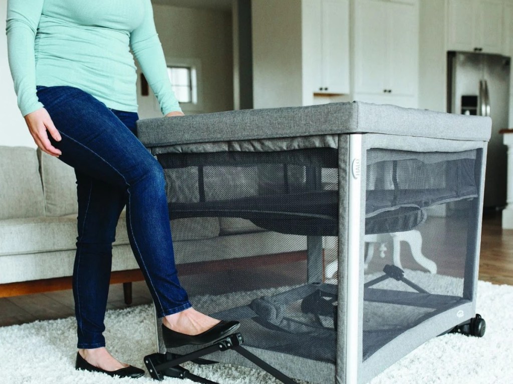 woman stepping on rocker attachment on gray bassinet