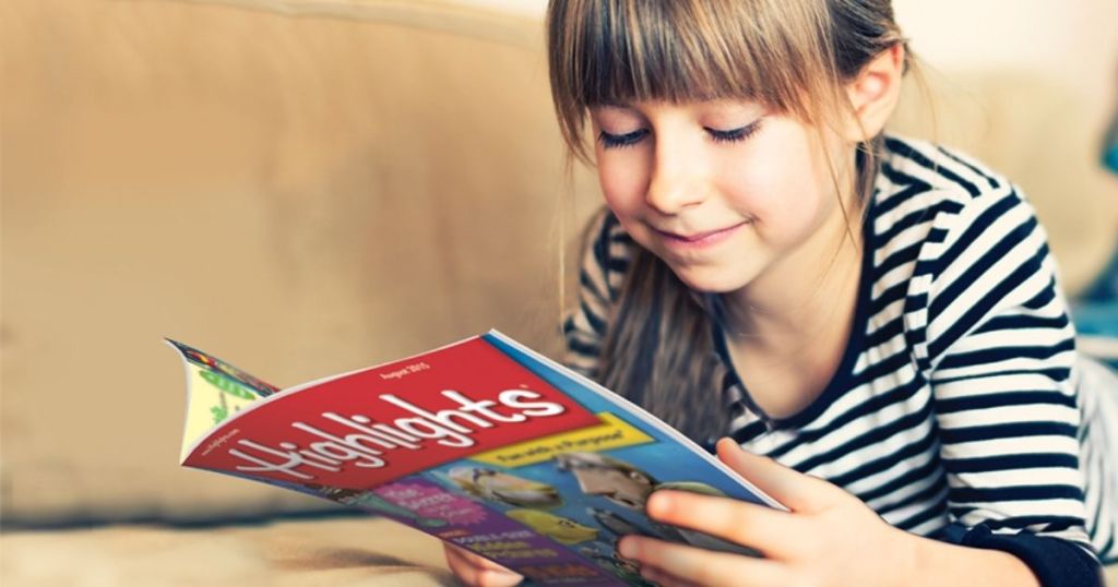 Little girl laying on stomach on couch reading magazine