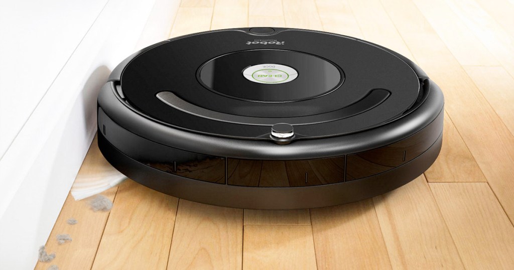 round black roomba robotic vacuum cleaning against baseboard on hardwood floor