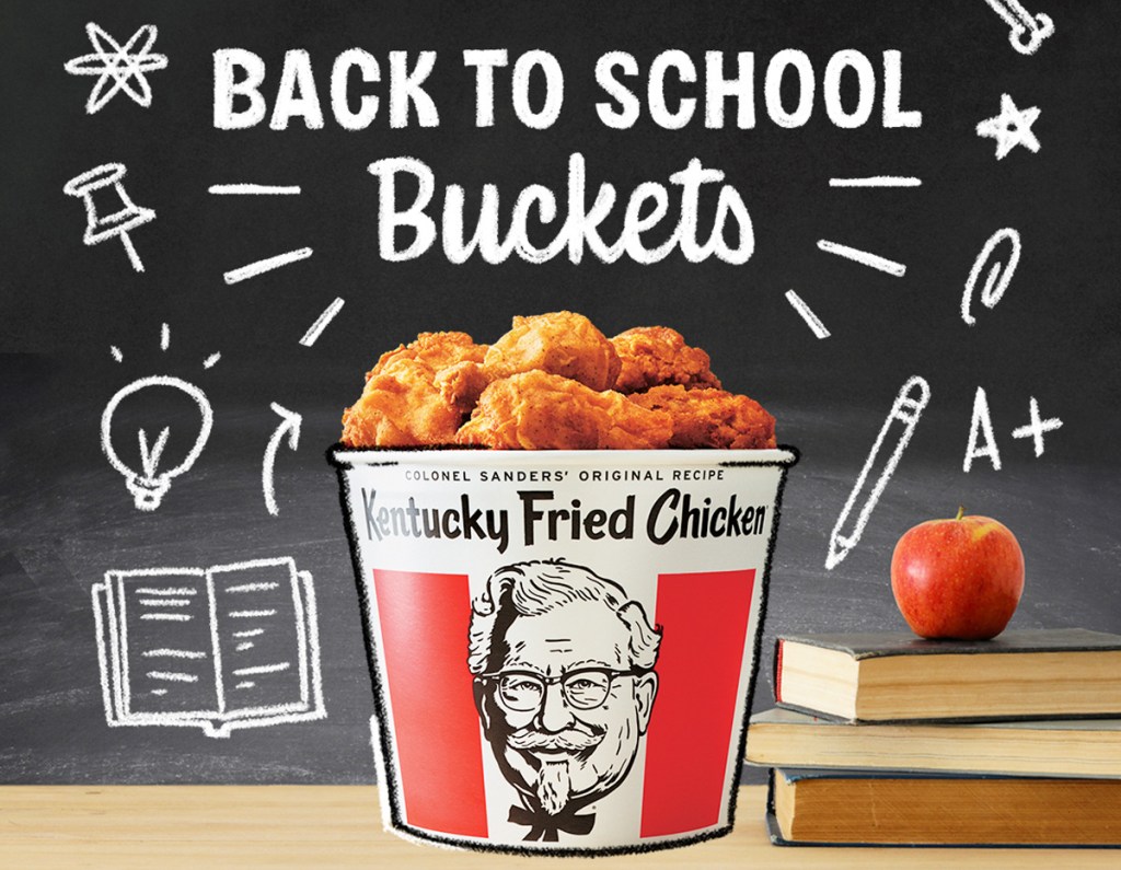 bucket of KFC fried chicken with stack of books, apple, and blackboard with school themed doodles behind it