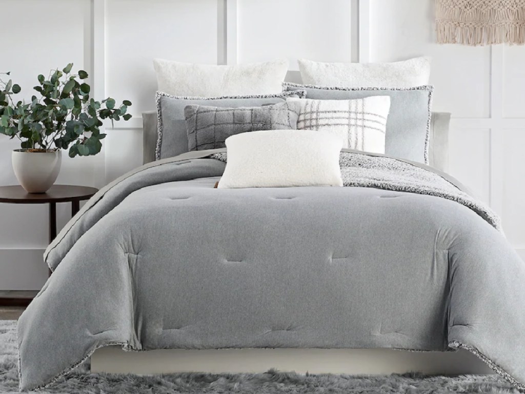 light grey cozy bedding and shams on a queen size bed next to a side table with a plant