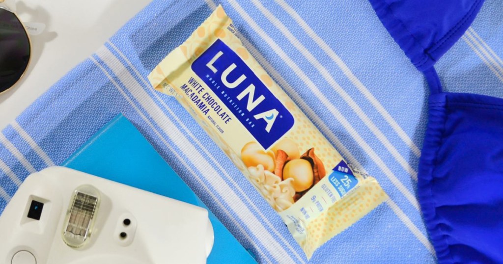 white chocolate macadamia snack bar on towel, bathing suit, camera, and sunglasses