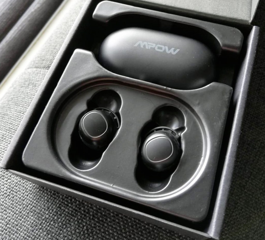 black wireless earbuds with charging case inside of box on grey couch