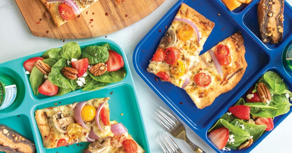 2 colorful nordic wear food trays filled with food next to a cutting board