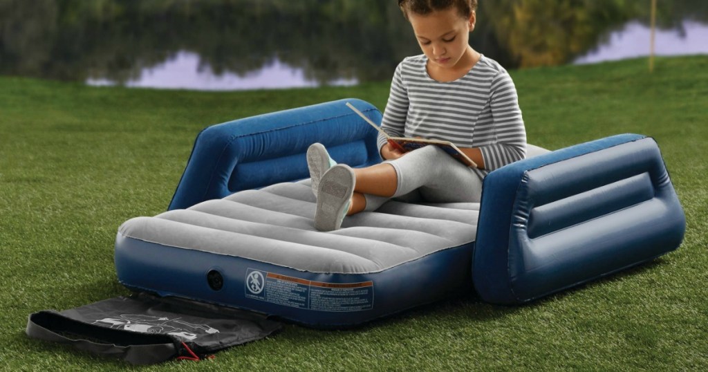 Young girl reading a book sitting on an air mattress in the grass