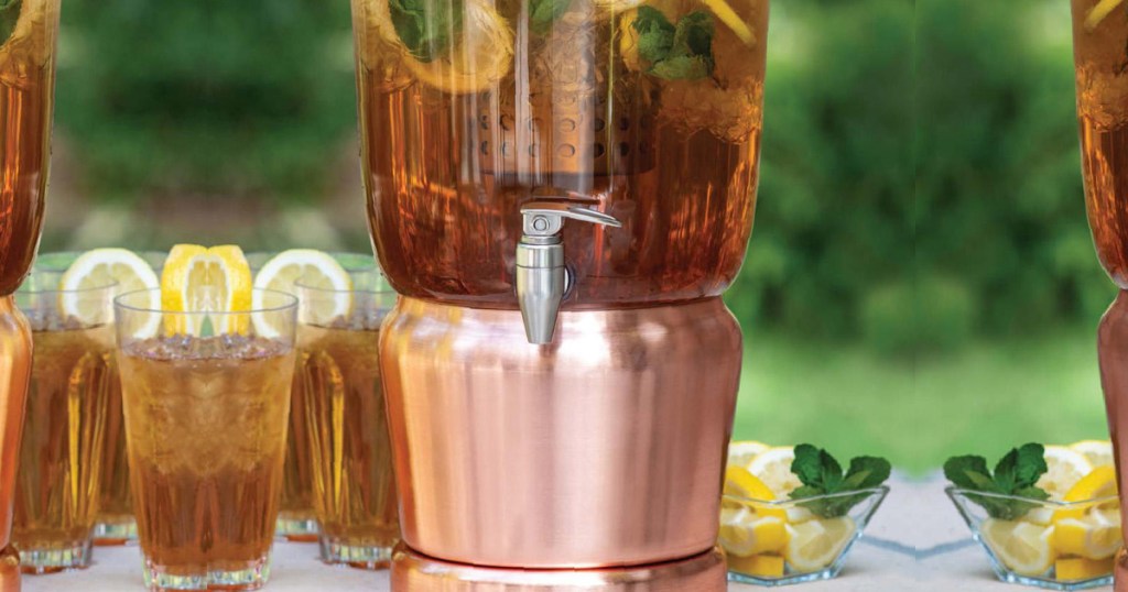 large copper beverage infuser sitting next to glasses of iced tea and lemons