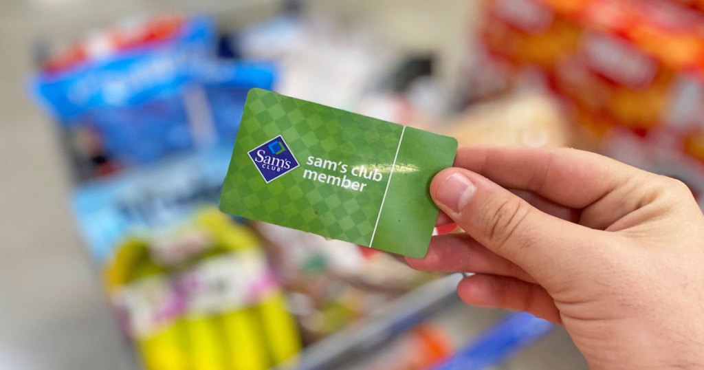person holding up a green Sam's Club membership card in front of full shopping basket