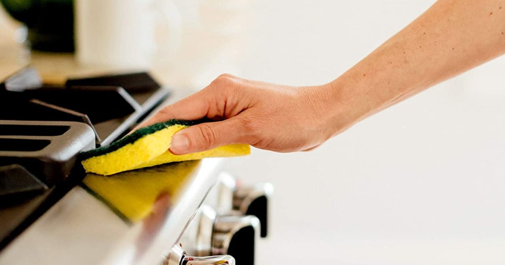 hand holding a scotch brite heavy duty sponge wiping down a kitchen stove replace household items