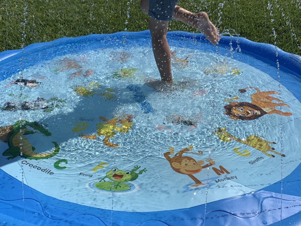 small child standing and splashing in a bright blue splash pad filled with water