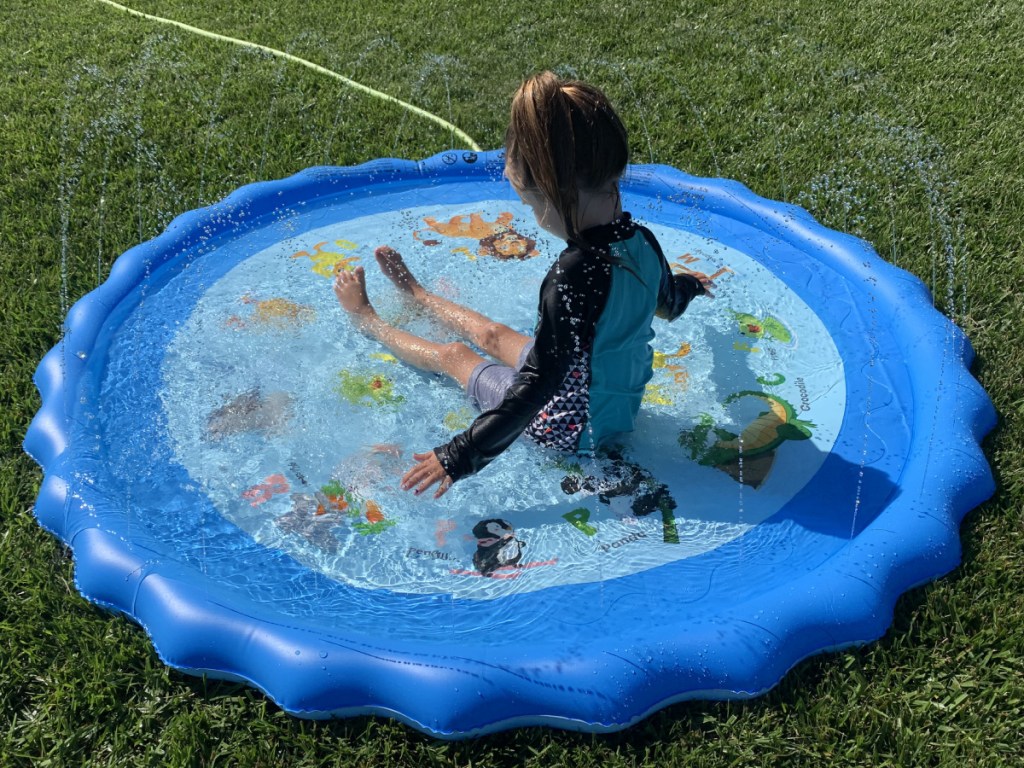 little girls sitting on a bright blue alphabet splash pad filled with water