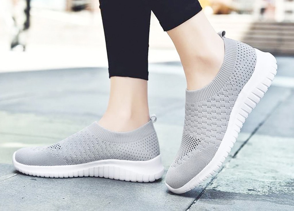 woman wearing a pair of light grey slip-on shoes walking outside