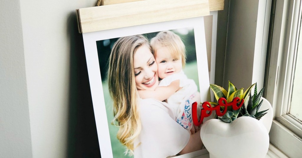 photo of a woman hugging baby on a wood hanger board with potted plant in front of it