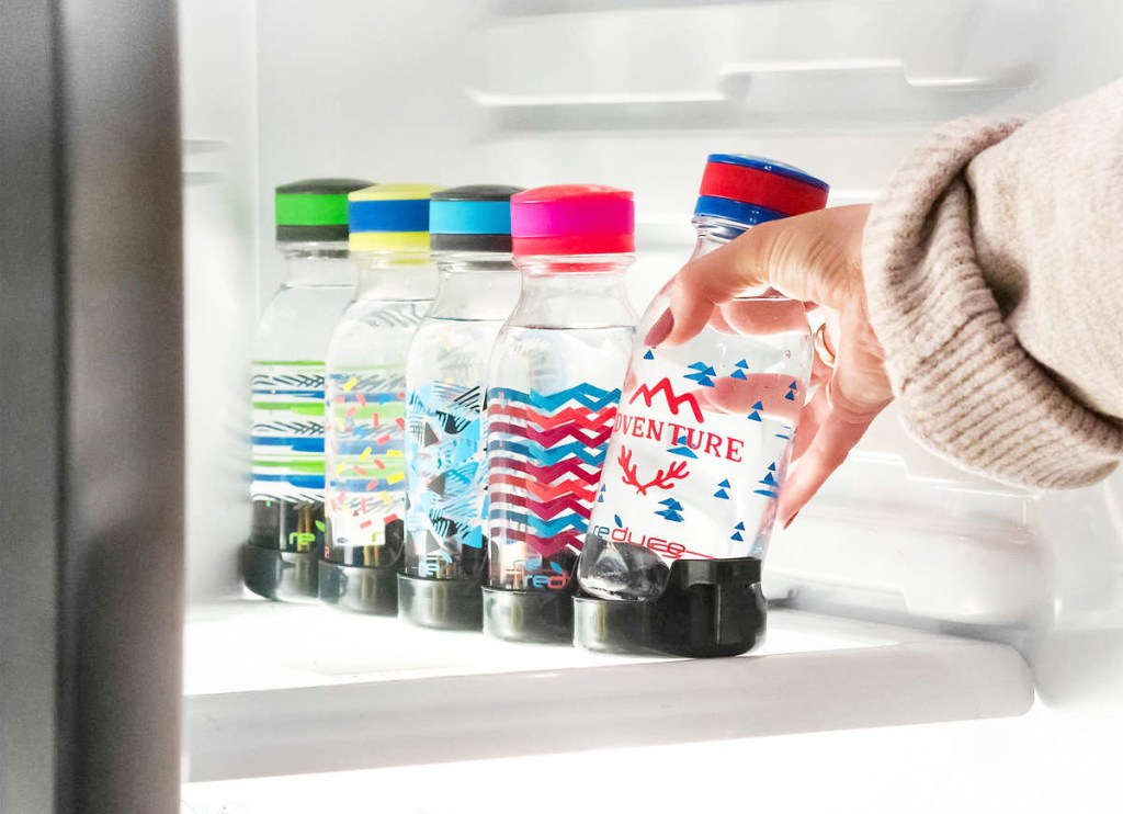 person reaching hand into fridge to grab a red and blue printed water bottle