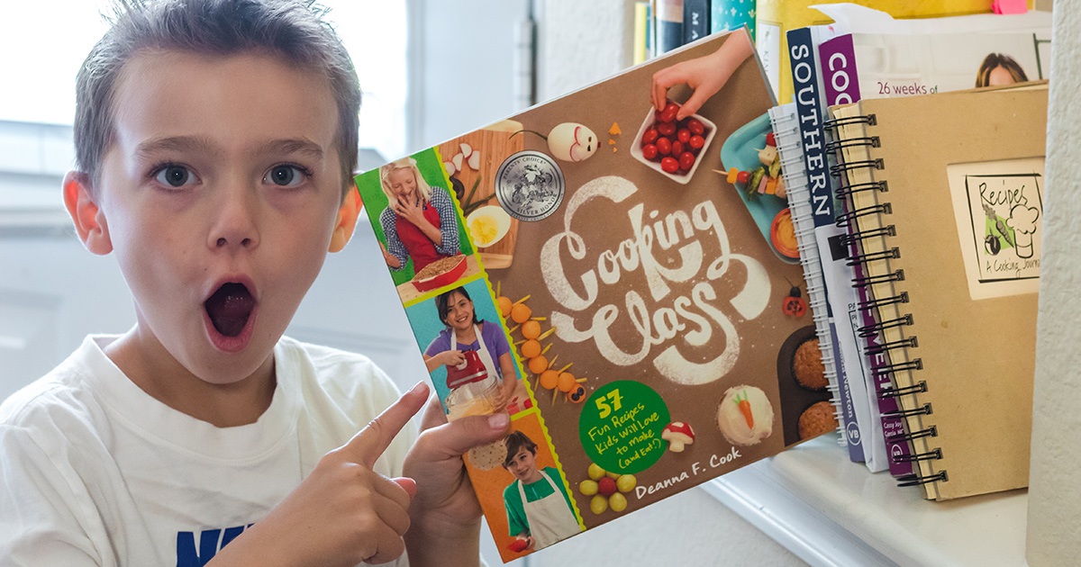 young boy holding cooking class cookbook for kids