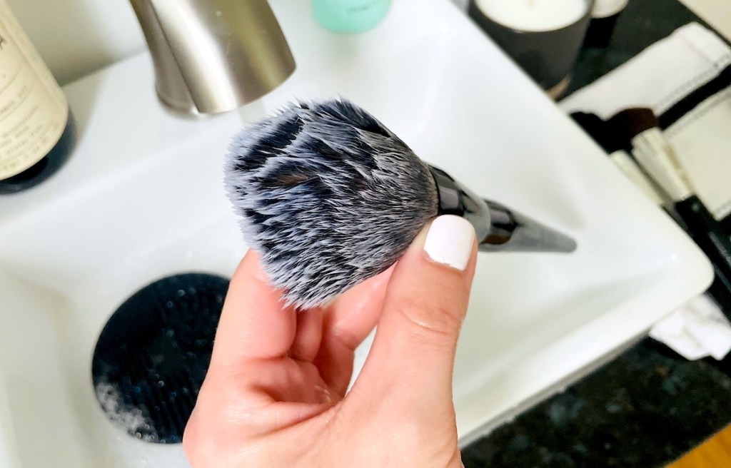 close up of hand holding makeup brush over sink