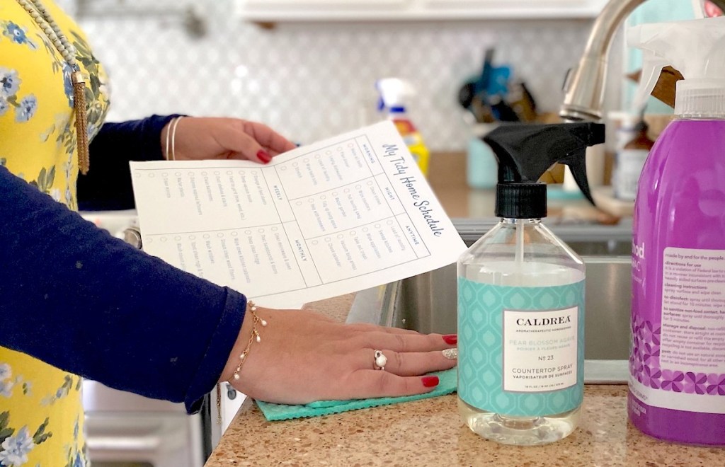 woman holding printable chore chart while wiping countertop