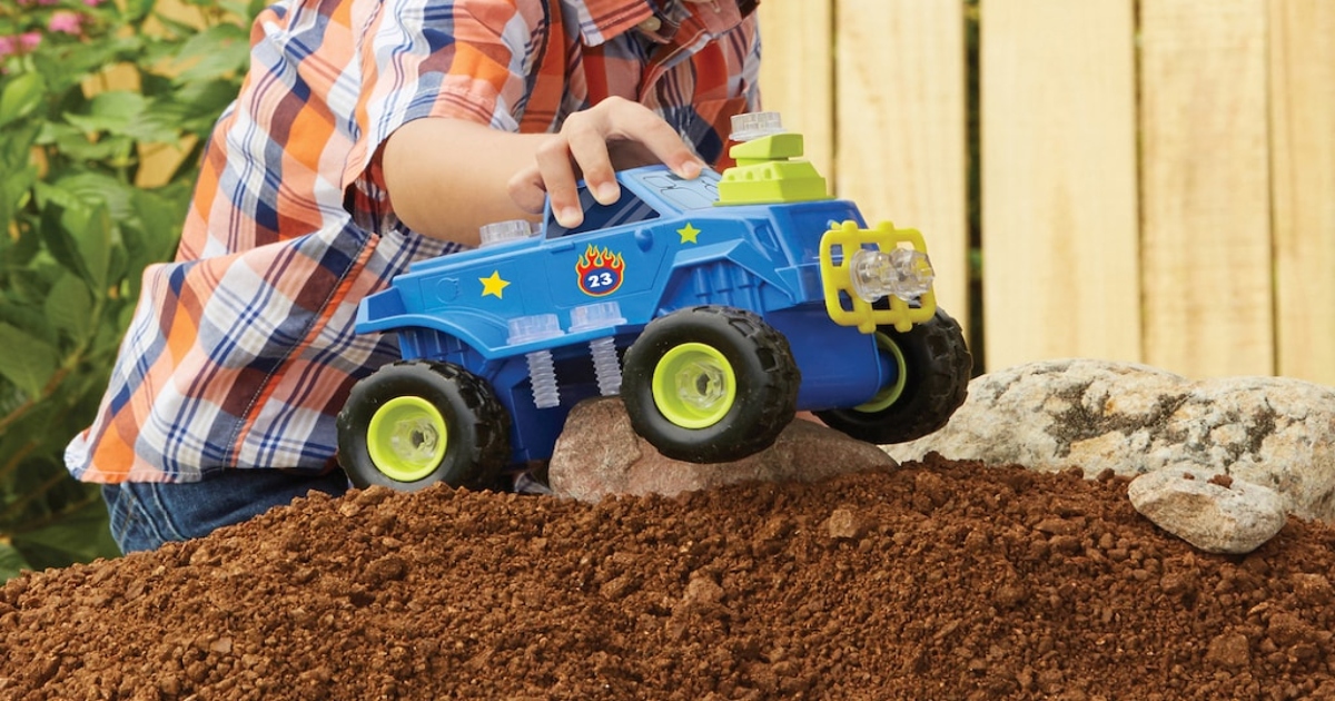 boy playing with blue monster truck on a pile of dirt