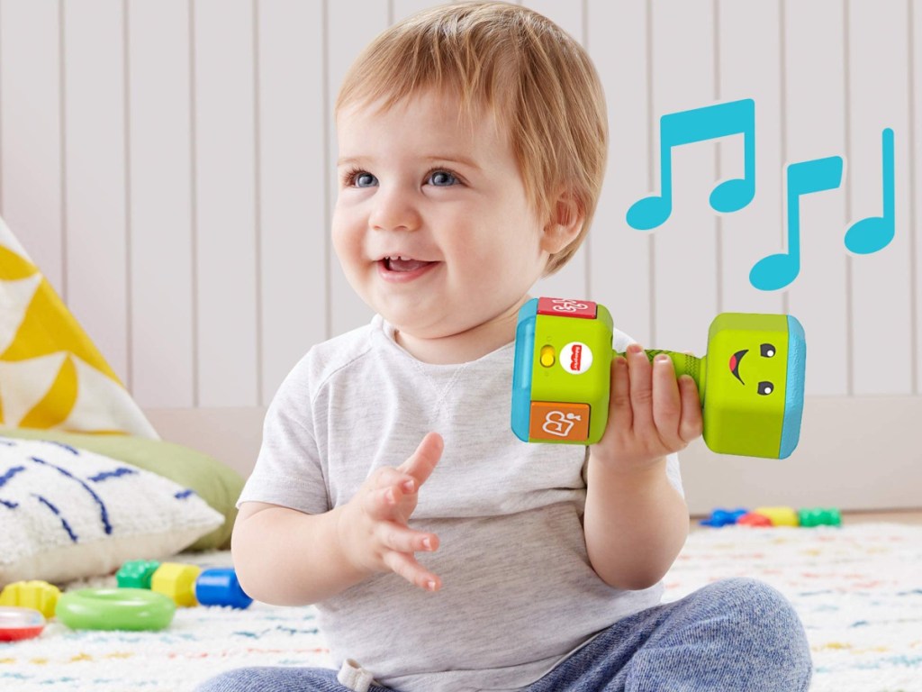 baby sitting on the flooring holding a musical green dumbbell