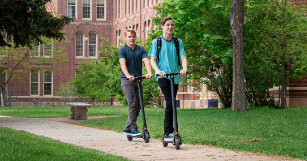 kids using electric scooter with school in background